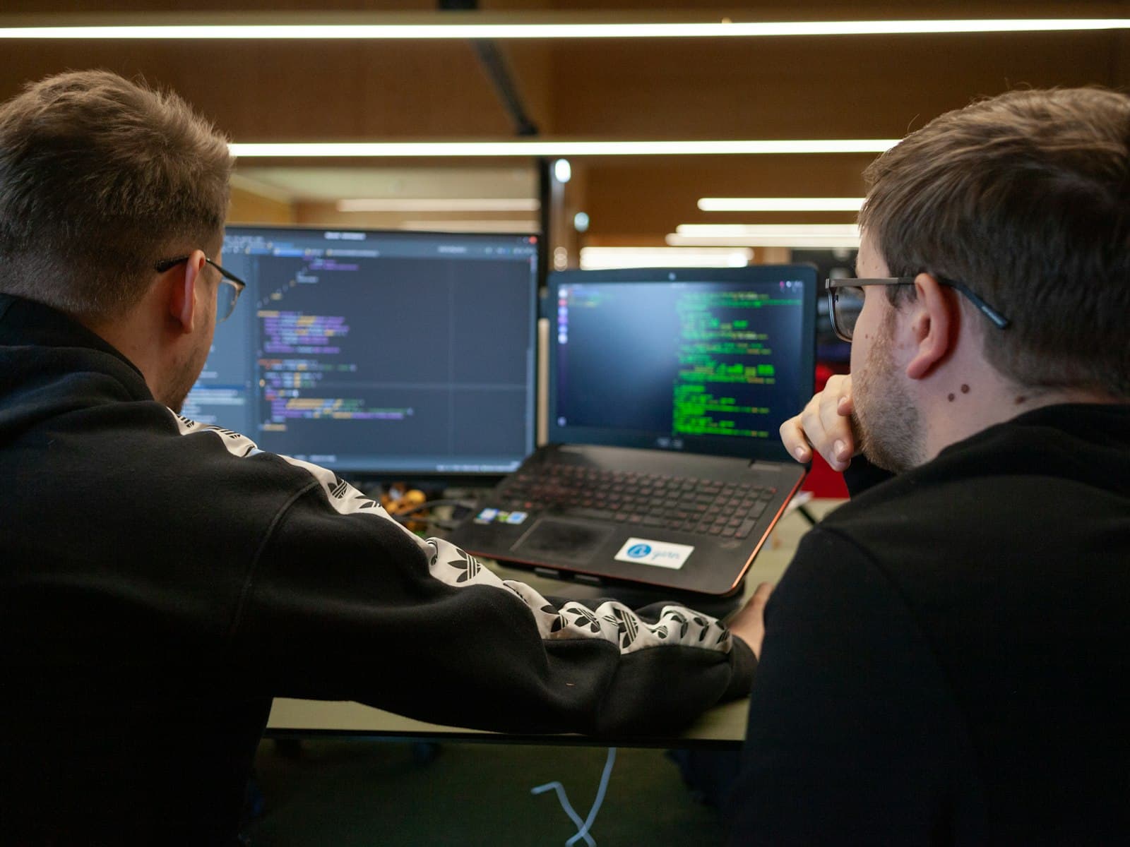 Twee developers bekijken samen code op twee schermen