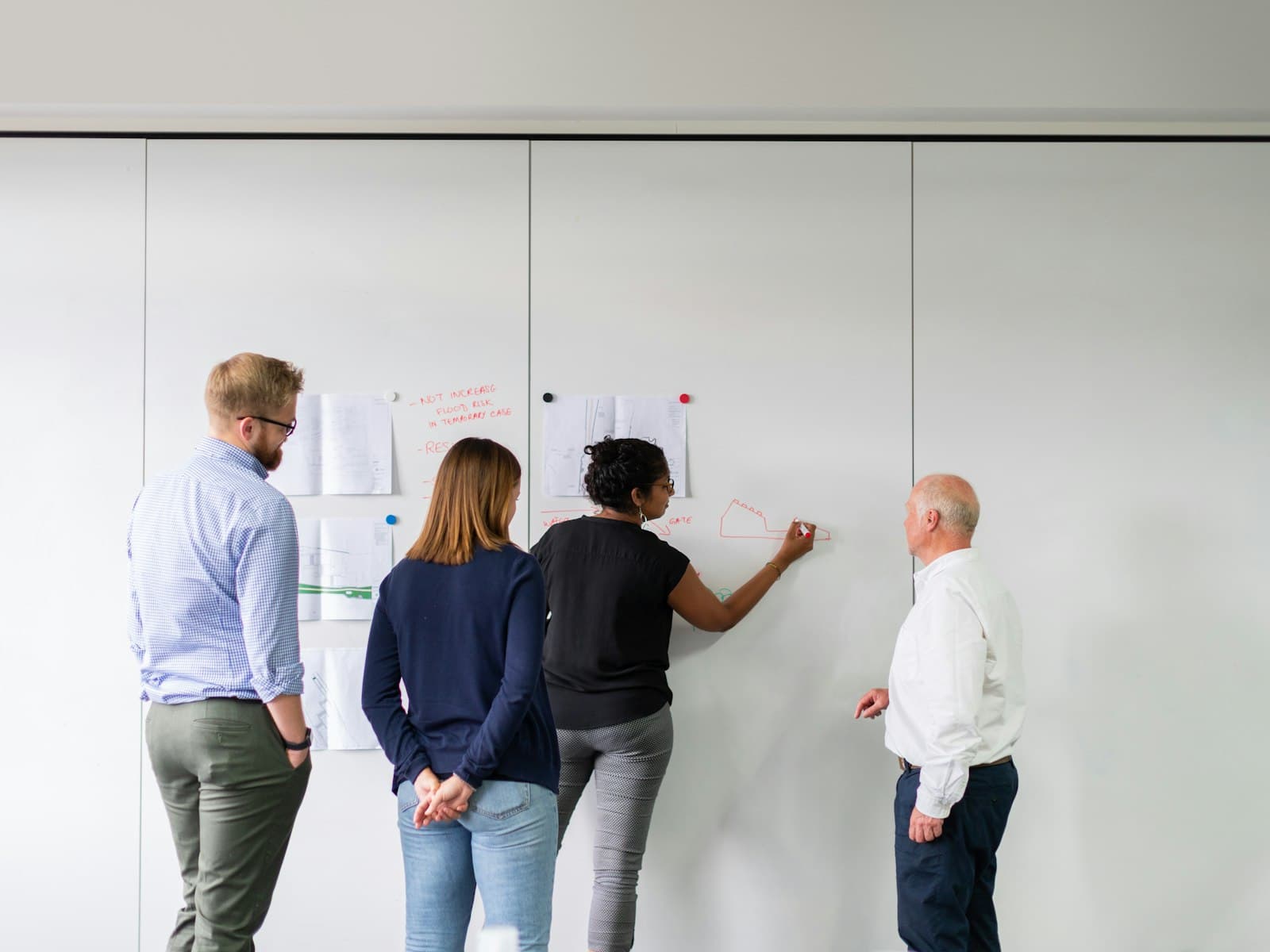 Business analist tekent op een whiteboard tijdens een werksessie met drie collega's